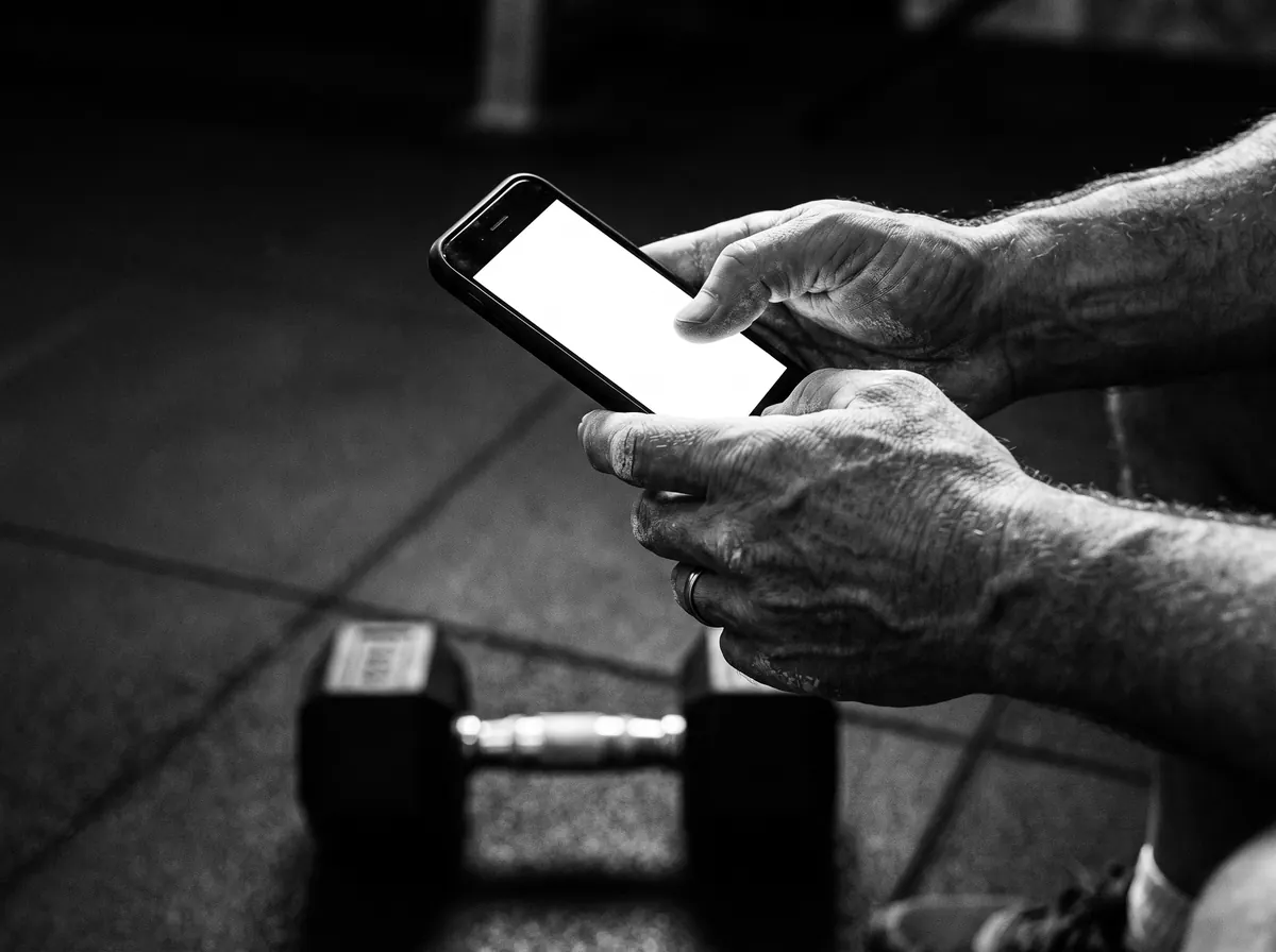 Hands logging a set on a phone, a dumbbell on the floor below